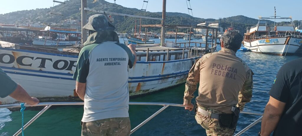 Foto de um agente temporário ambiental e um da Polícia Federal vistoriando uma embarcação