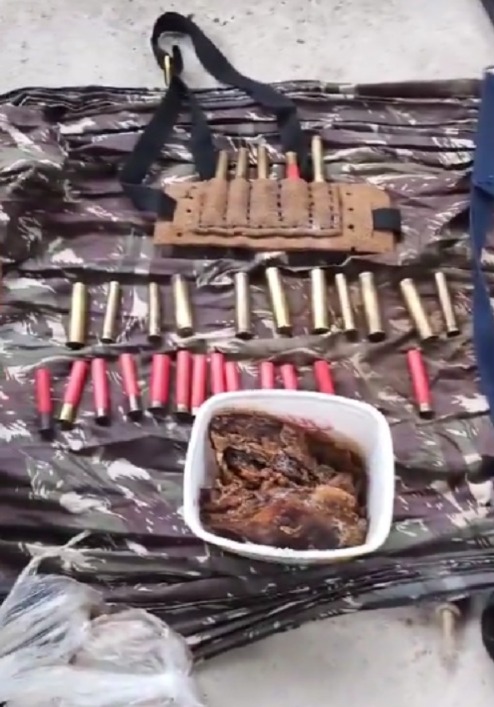 Foto mostra cartuchos colocados no chão ao lado de um pote, aparentemente, contendo carne